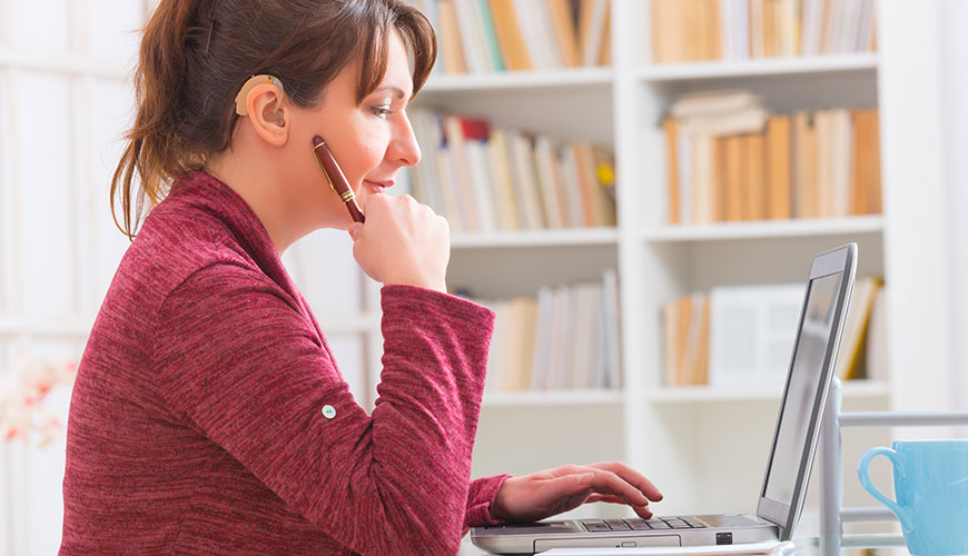 A person with a hearing aid sits working at a laptop