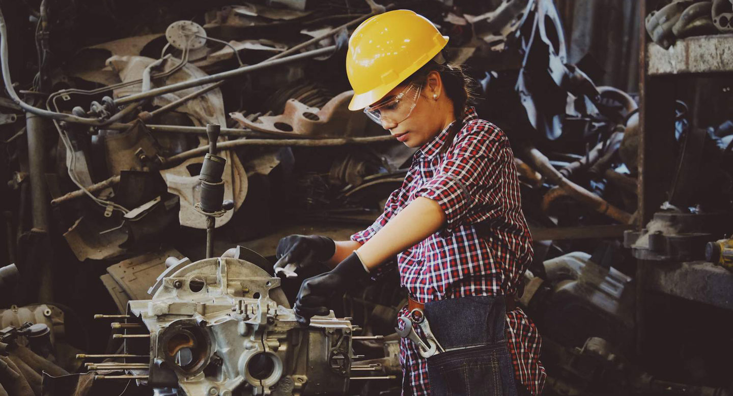 Woman Wears Yellow Hard Hat Holding Vehicle Part