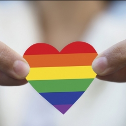 Fingers holding onto a cut out rainbow coloured heart 