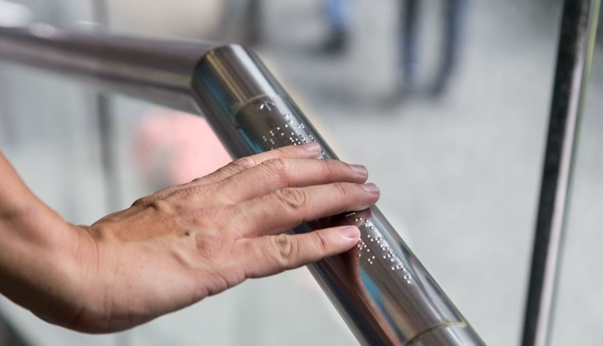 Image of a hand reading braille on a railing 