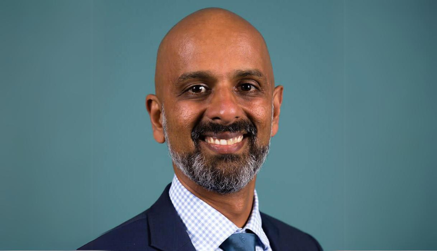 Photo of Commissioner Giridharan Sivaraman, smiling and looking towards camera with blue background