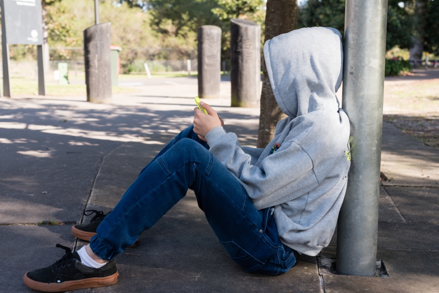 Side View Of Teenage Boy Using Phone While Sitting On Footpath