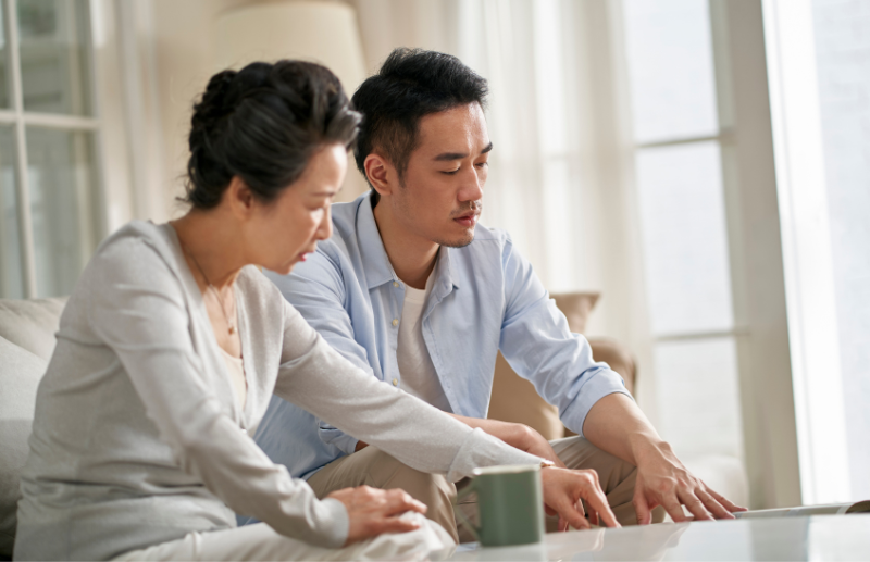 A man and his mother seated on the couch looking over papers on the coffee table