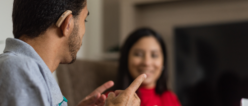 A person with a hearing aid engaging in a conversation with another person. 