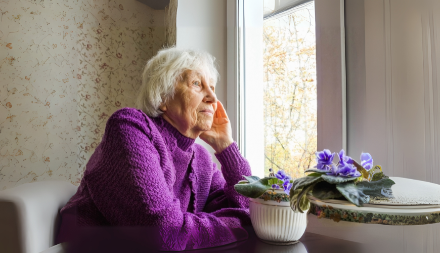 older woman in purple jumper look out a window