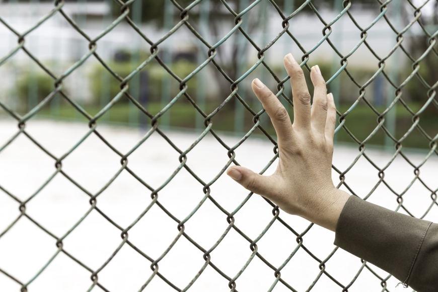 A woman's hand holds onto the fencing of a detention facility