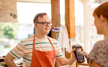 A young person with a disability wears an apron and serves a customer at a 