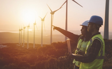 Two workers in discussion with wind farm in background