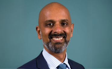 Photo of Commissioner Giridharan Sivaraman, smiling and looking towards camera with blue background