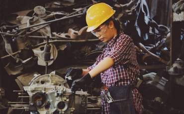 Woman Wears Yellow Hard Hat Holding Vehicle Part