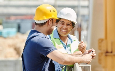 A smiling woman and a man work on a construction site.