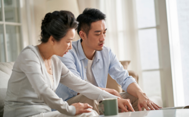 A man and his mother seated on the couch looking over papers on the coffee table