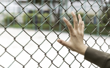 A woman's hand holds onto the fencing of a detention facility