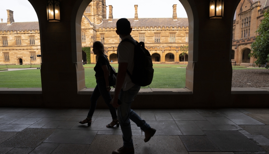 Image of shadowed university students walking through open corridor alongside university quadrangle