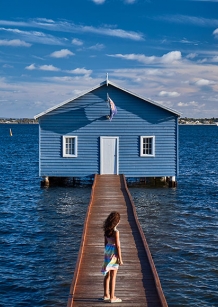 A girl standing on bridge surrounded by water and a house in front