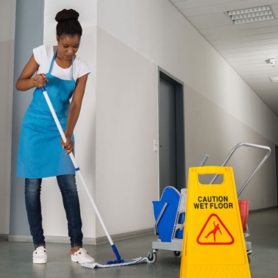 Cleaner in office building with a 'caution wet floor' sign