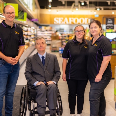 Dr Ben Gauntlett sits in a wheelchair in a Woolworths store with three Good Sammy staff standing around him.