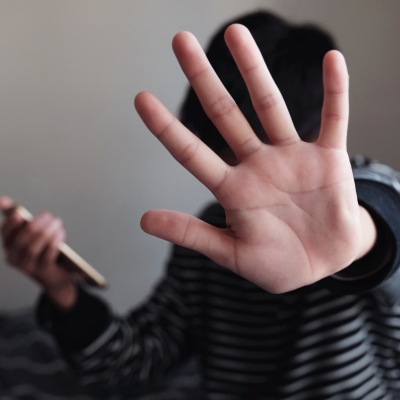 Teenage Asian boy holding a smartphone and showing a stop sign with his hand.