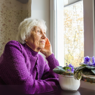 older woman in purple jumper look out a window