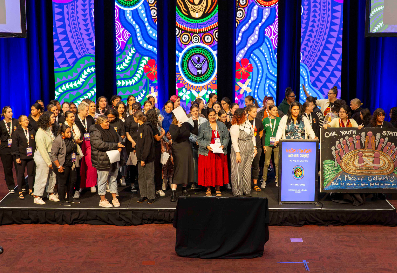 A large group of young First Nations women on stage, presenting a Youth Statement.